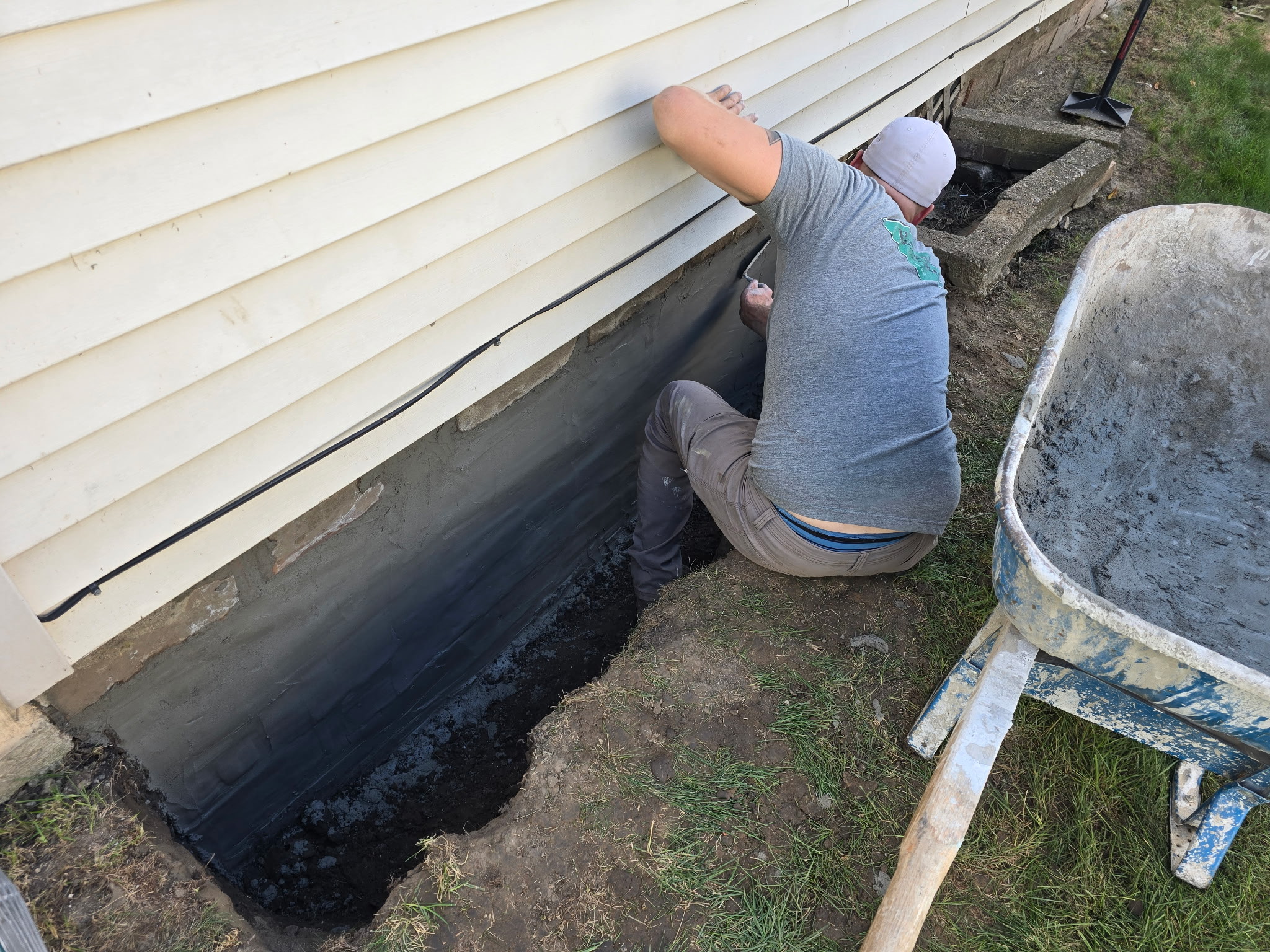 Worker parging a waterproofed exterior foundation wall in a dug trench