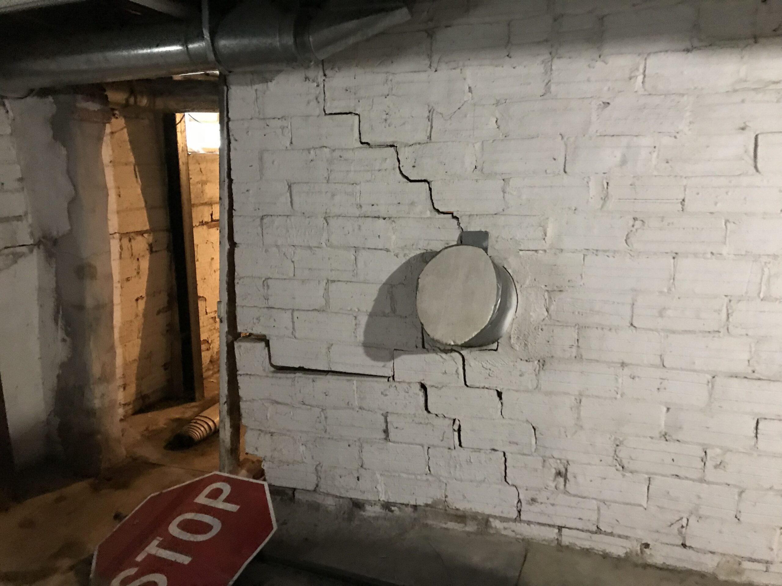 A stair-step crack running through a brick basement wall at a corner