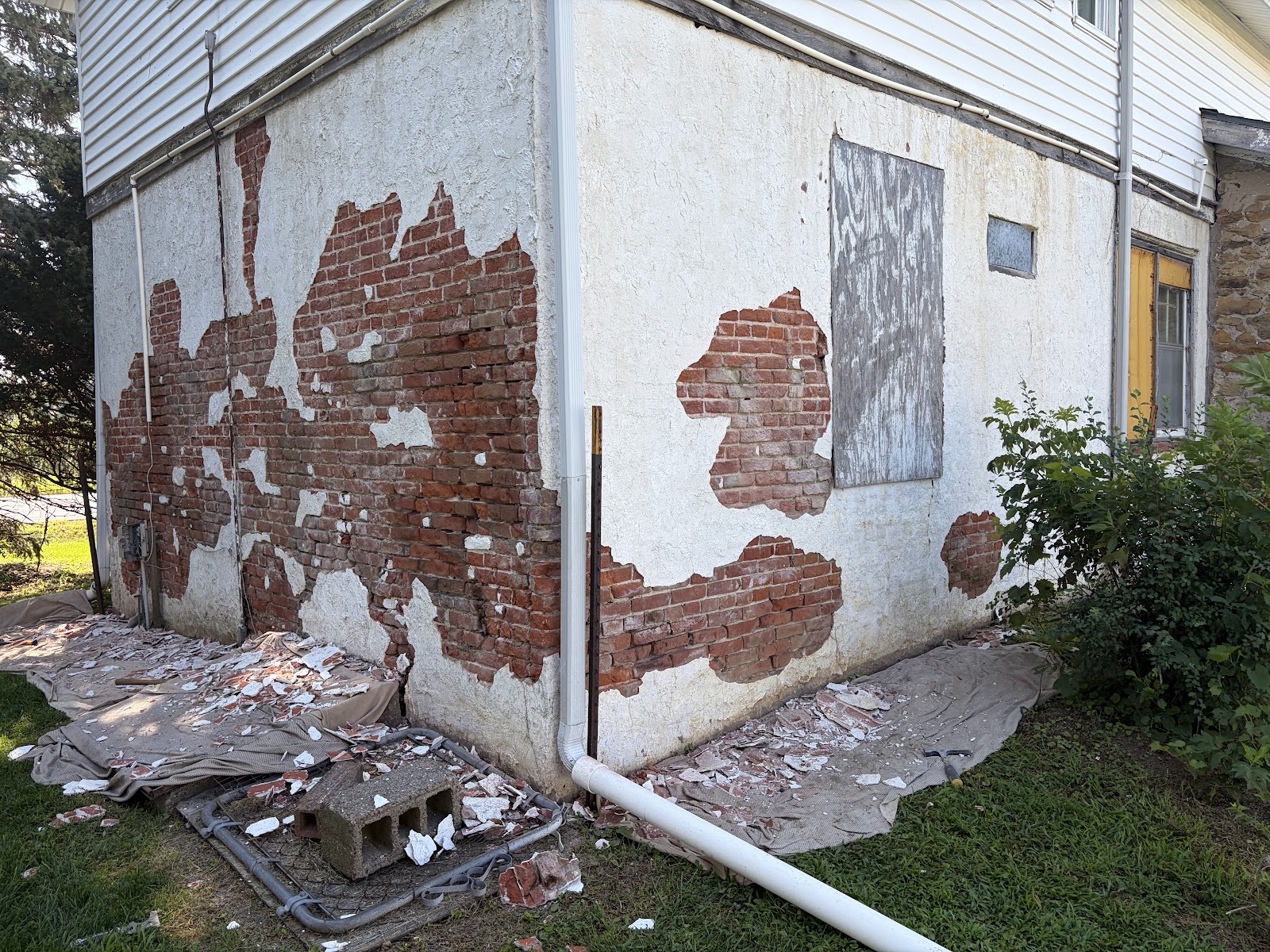Before the repair — deteriorated stucco had separated from the brick masonry beneath, leaving bare brick exposed and failed material at the base of the wall