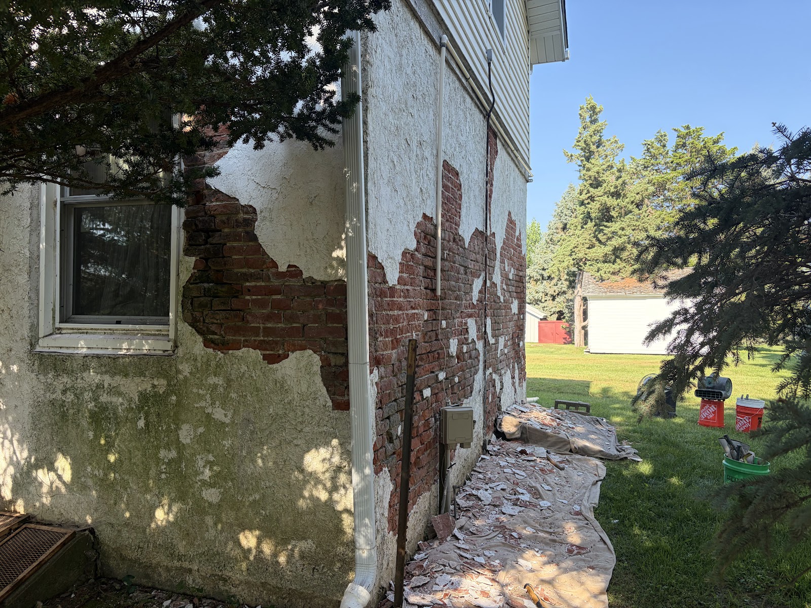 Failing stucco along the side elevation, exposing the brick substrate underneath