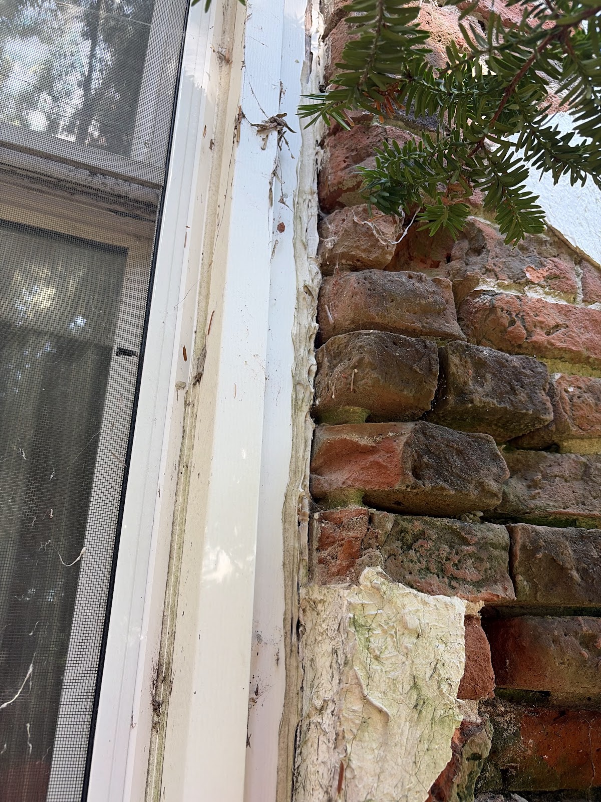 Close-up at a window edge where the failing stucco was removed, showing the brick and stone masonry substrate behind the finish