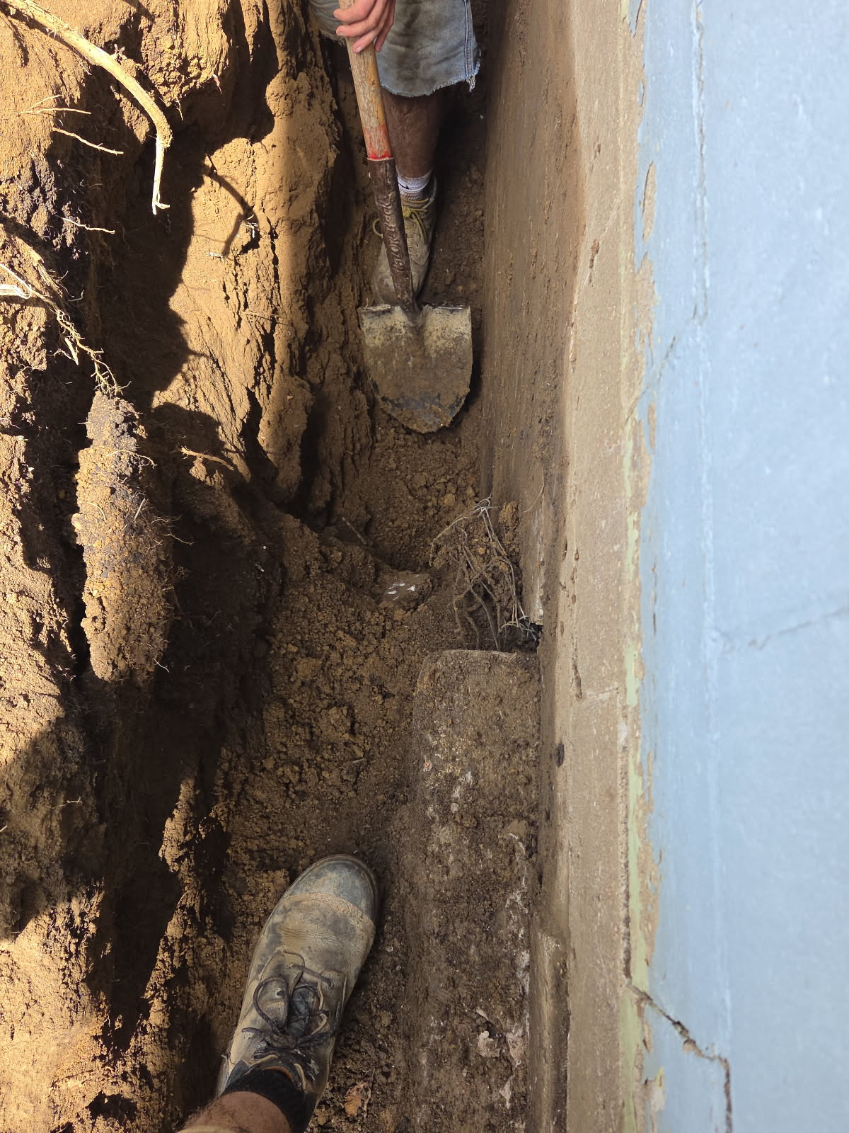 Narrow trench dug down toward footing depth for the downspout drainage line