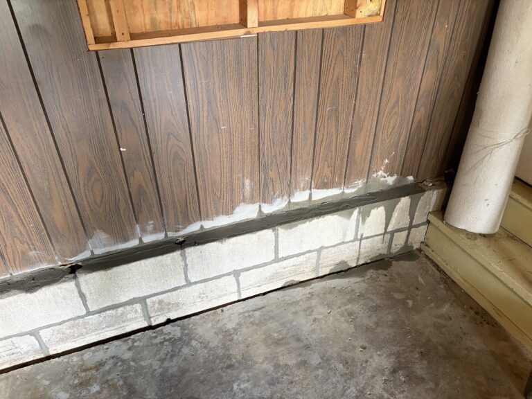 Completed exterior repair — rear garage concrete block wall with fresh mortar joints and a rerouted downspout, Davenport, Iowa