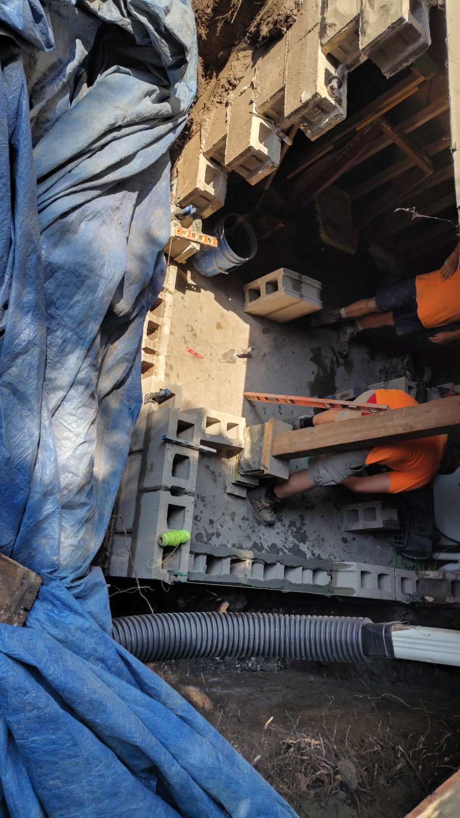 Work area with block staged, bracing lumber and drain pipe alongside the open excavation