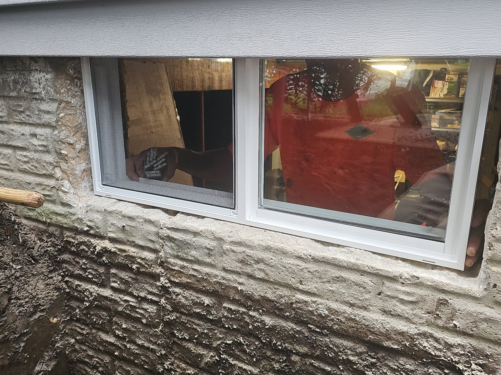 New double-sliding basement window set into the stone foundation opening, seen from outside