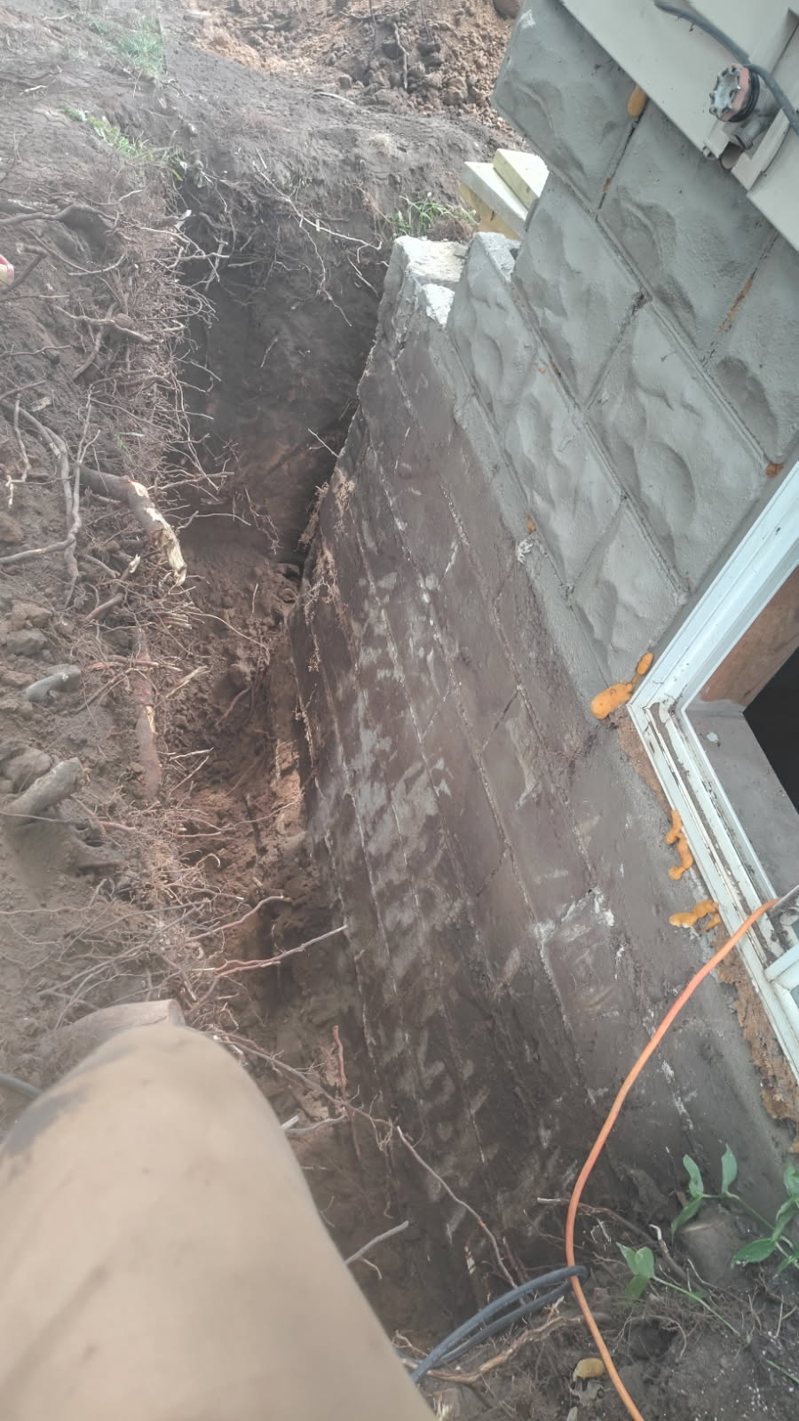 Rebuilt concrete block foundation wall with fresh mortar joints exposed in the excavation