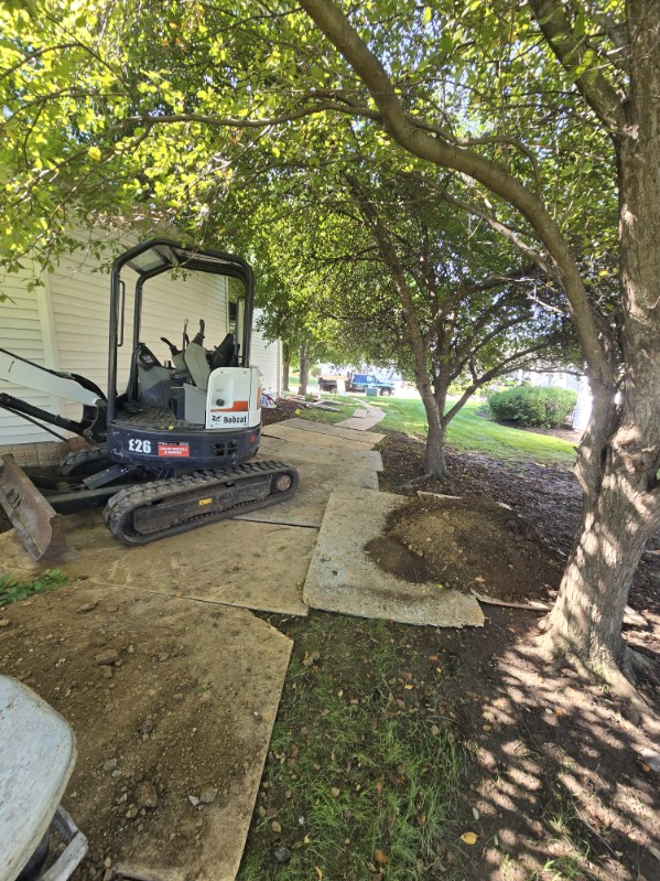 Compact excavator digging the egress window well next to the home