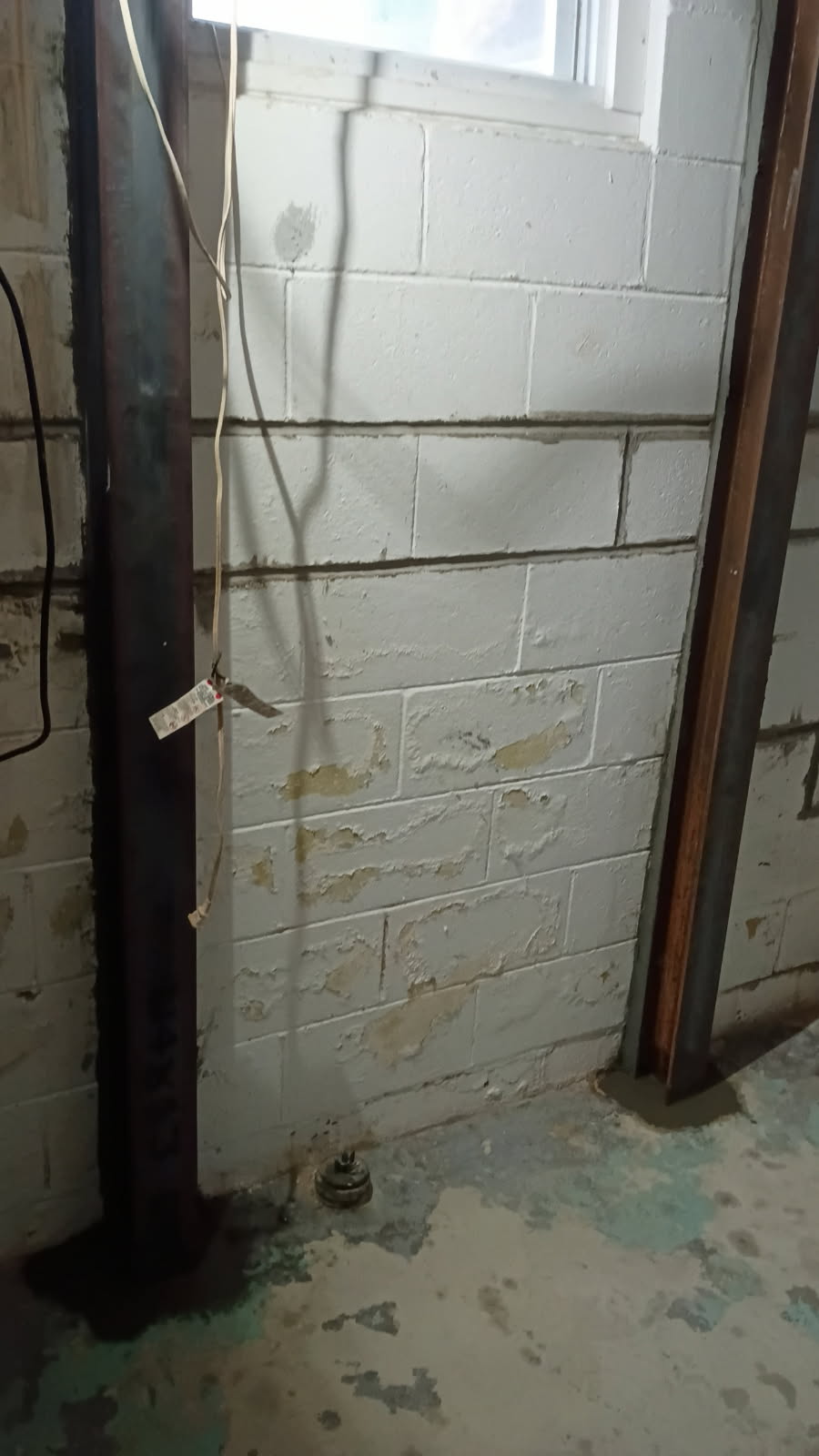 Two steel I-beam braces installed on a block wall beside a basement window
