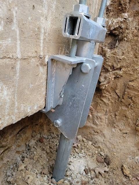 Close-up of a galvanized helical pier bracket bolted to the side of a concrete foundation