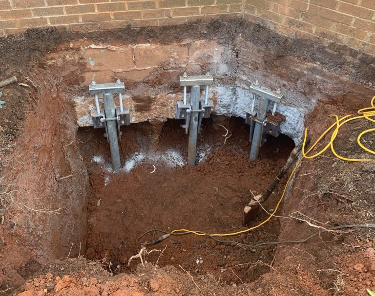 Three helical piers with brackets installed under a brick foundation in an excavated pit