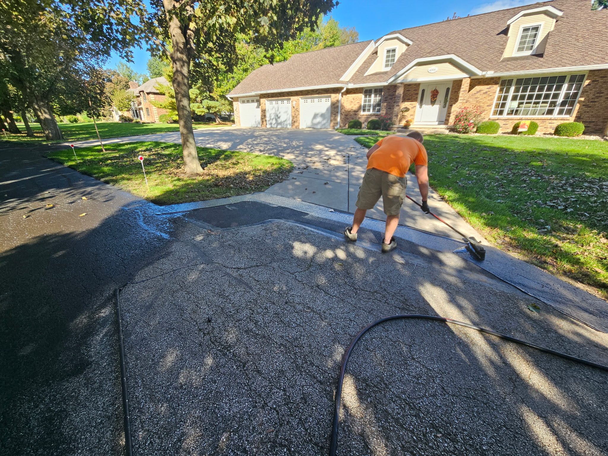 Crew member applying sealer near the house edge of the driveway
