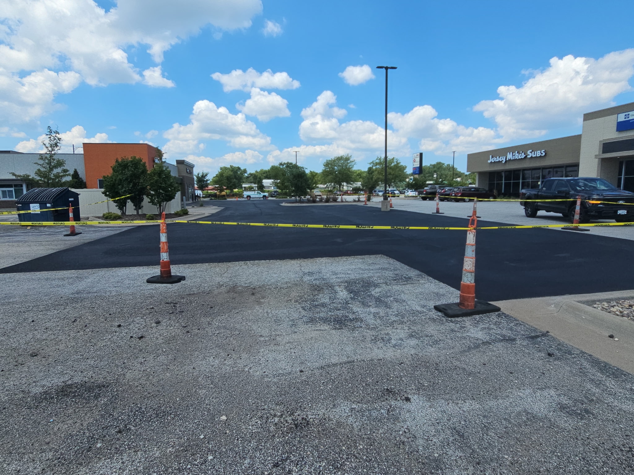 Cone line between freshly sealed black asphalt and the unsealed grey section of the Davenport lot