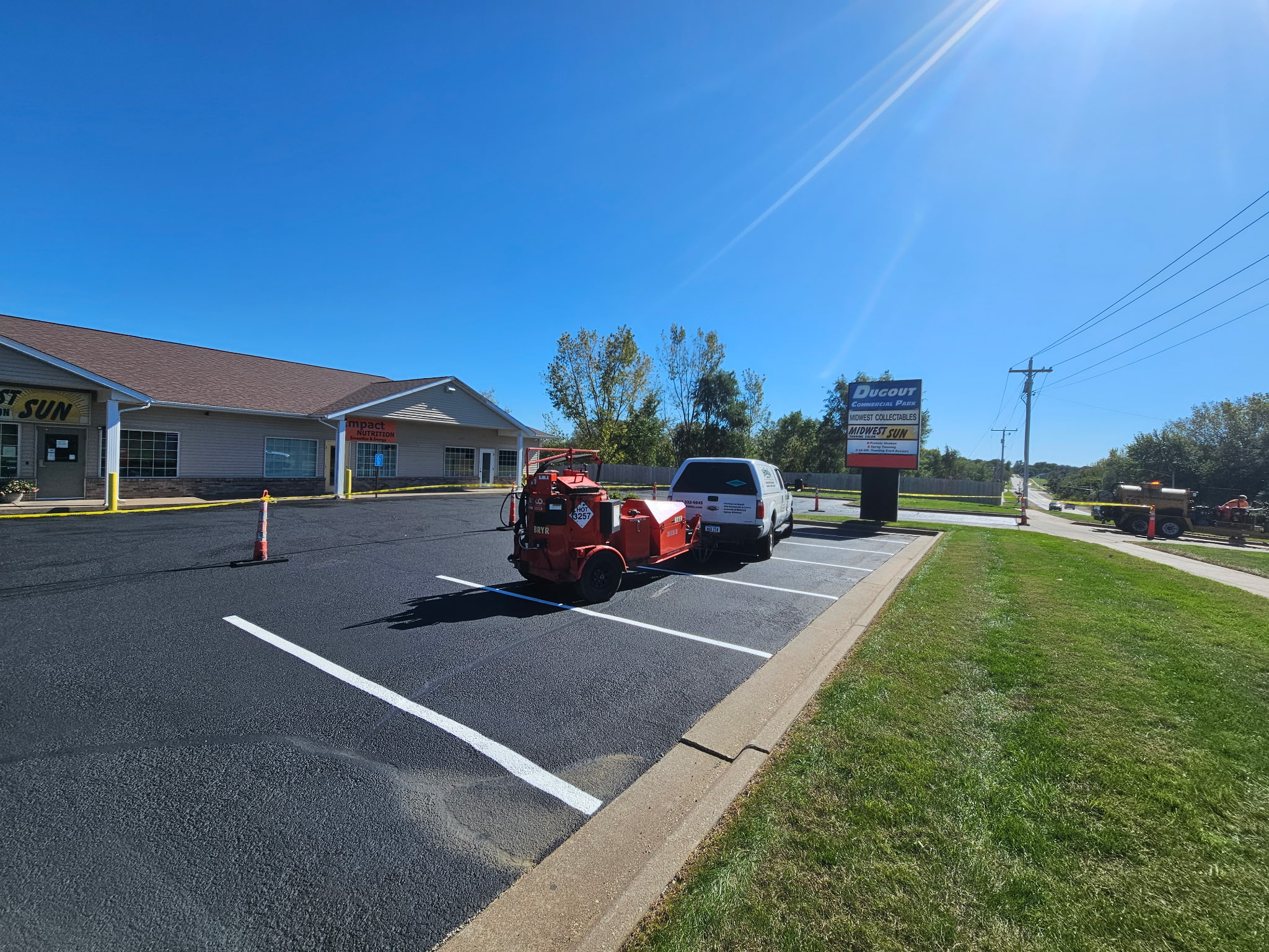 Behncke crew truck and sealcoating rig on the freshly sealed Davenport parking lot with new white line striping