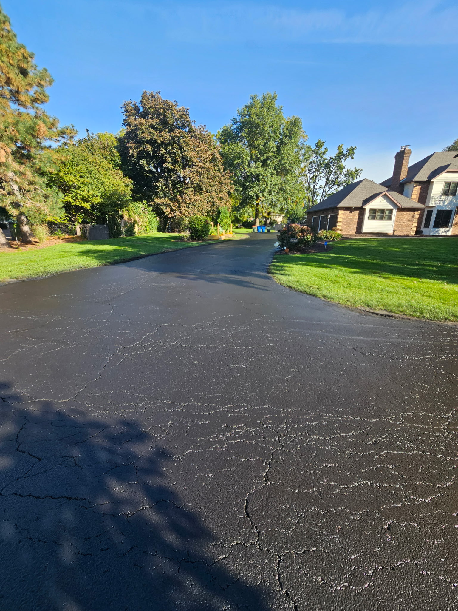 Sealcoated driveway curving toward the house with the new sealer still dark and even