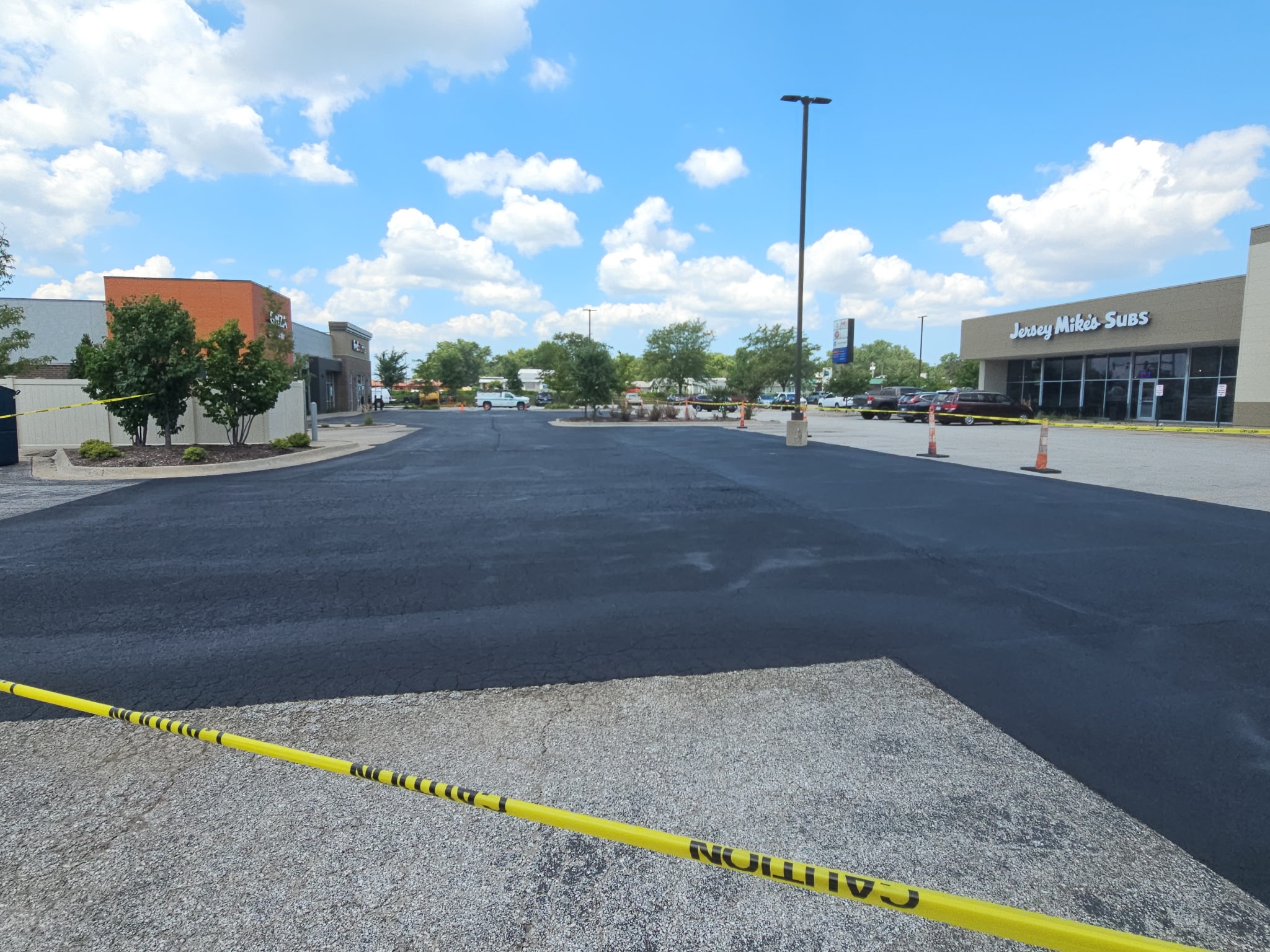 Finished sealcoated parking lot off Jersey Ridge Road behind caution tape with the storefronts in the background