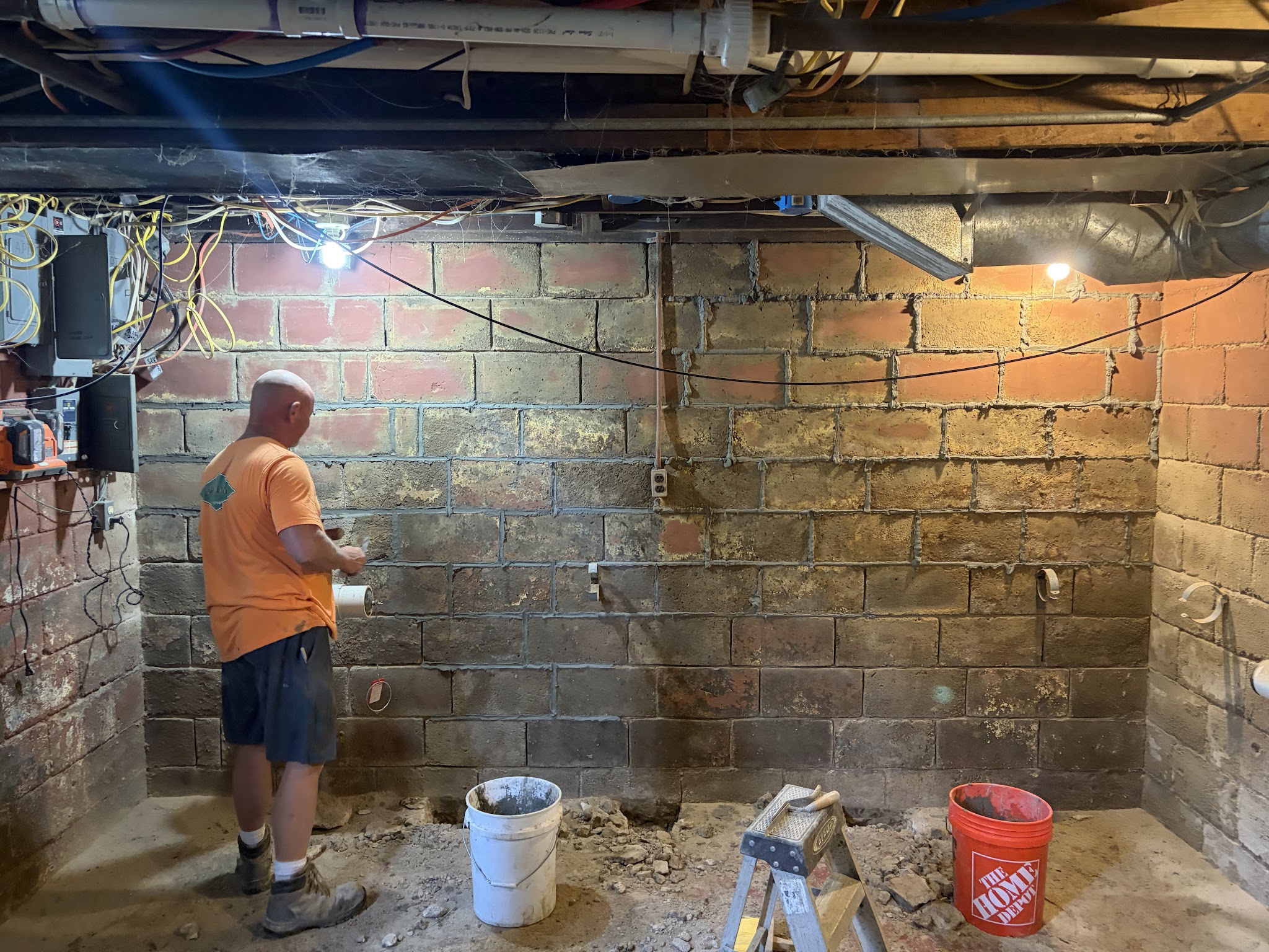 Crew member tuckpointing the interior block foundation wall beside a steel brace