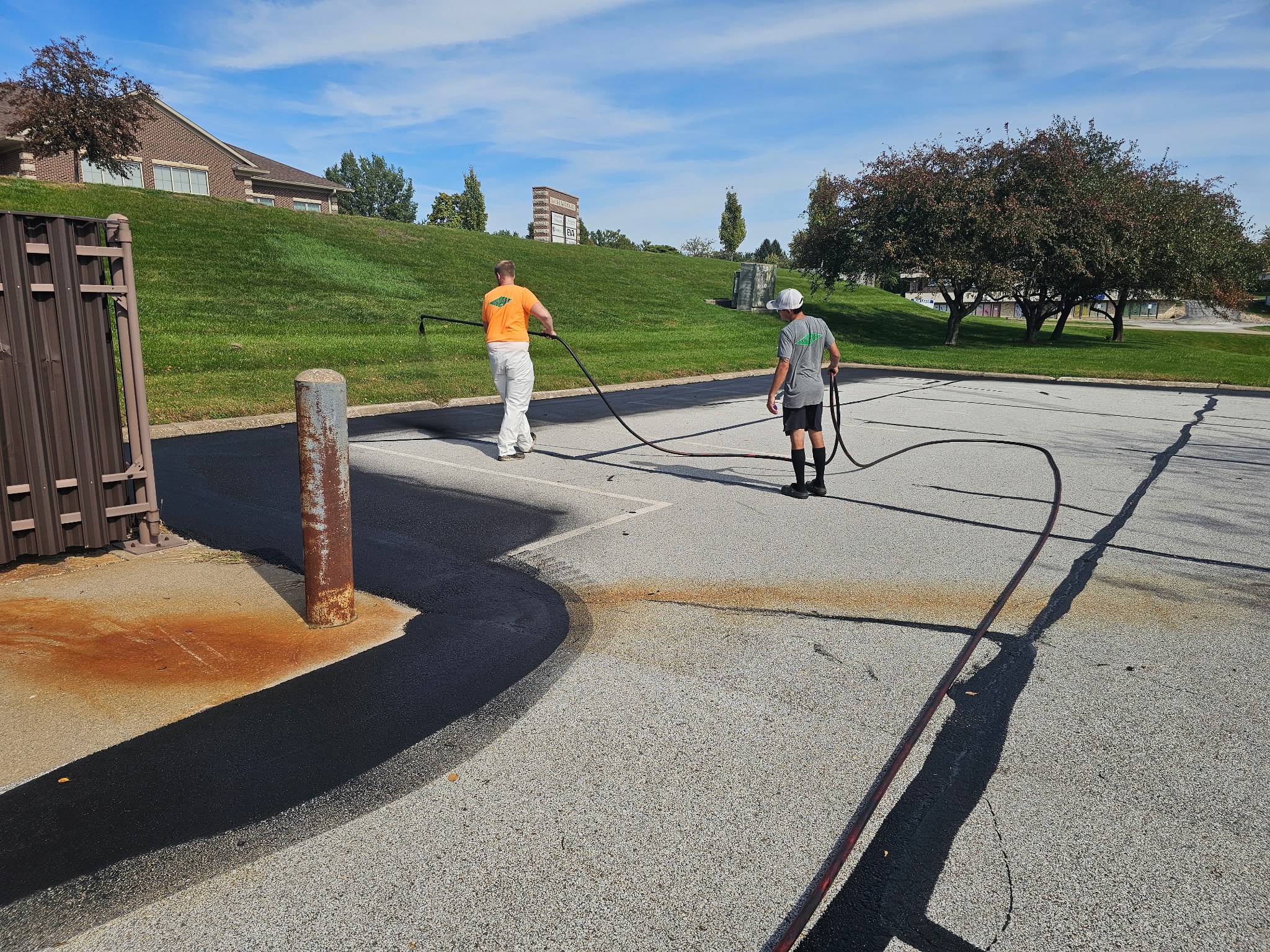 Two crew members spraying asphalt sealer across the Bettendorf parking lot
