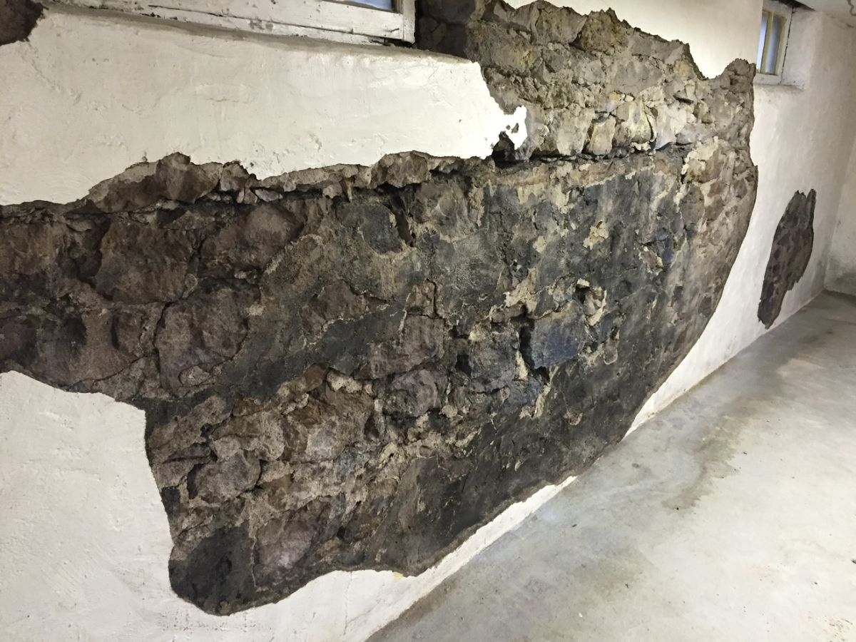 An old parge coat letting go and exposing the stone behind it.