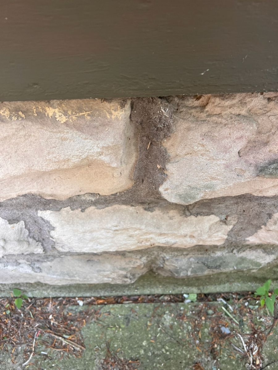 Washed-out, sandy mortar joints on the outside of a stone foundation.